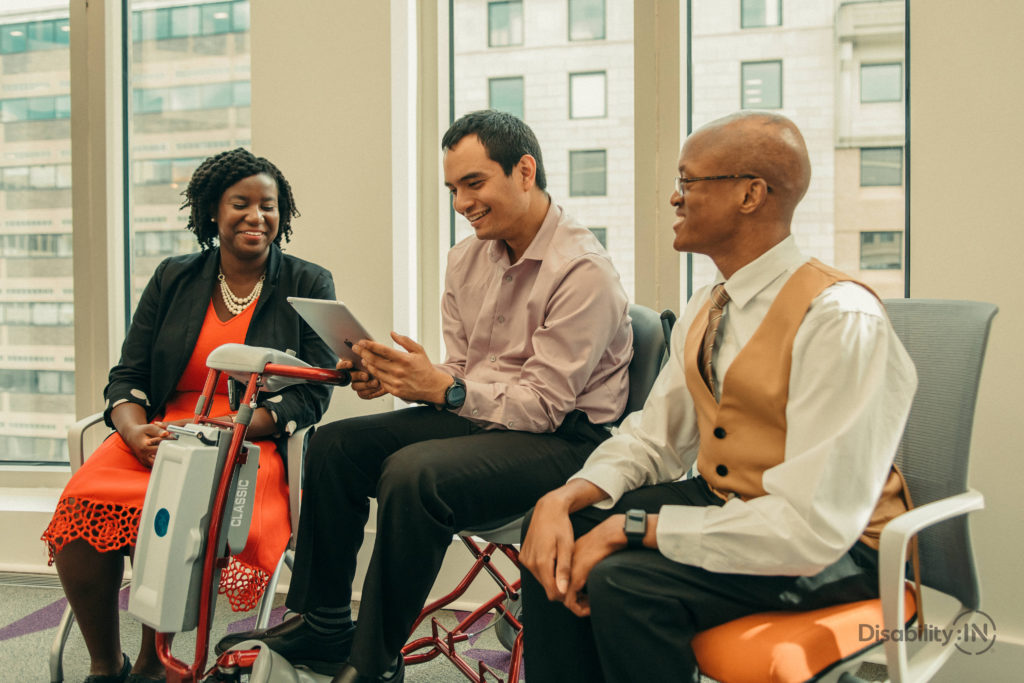 Workers sitting and smiling with employee who uses motorized scooter Workers sitting and smiling with employee who uses motorized scooter
