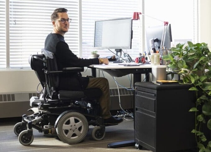 Man sitting in motorized chair at computer desk, part of NOD website banner
